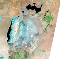 Satellite view of a fragmented pale-blue inland sea in tan desert, with an elongated dark remnant on the west and several separated northern pools.