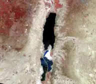 Satellite view of a long, narrow, nearly black lake in a pale desert rift, divided near its southern end by geometric evaporation ponds.