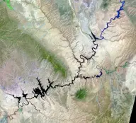 Satellite view of a dark branching reservoir filling a maze of narrow desert canyons, with long finger-like arms extending in many directions.