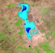 Satellite view of a bright turquoise, irregularly shaped salt lake surrounded by tan land and crossed near the middle by a thin causeway.