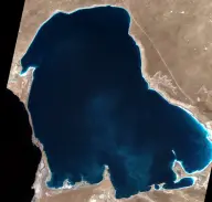Satellite view of a large dark-blue desert lagoon connected to a much larger sea by an extremely narrow channel at the western edge.