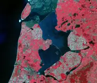 False-color satellite view of dark enclosed water divided by long straight dikes and surrounded by precisely rectangular red and green farmland.