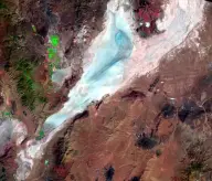 Satellite view of a long pale-blue dry lakebed enclosed by brown desert mountain ranges, with a darker curved edge along one side.