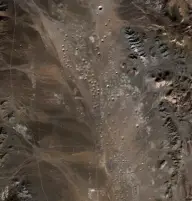 Satellite view of an arid brown basin densely pocked with dozens of small circular craters, bordered by rocky ridges.