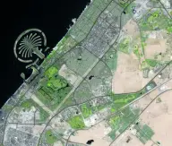 Satellite view of a palm-tree-shaped artificial island enclosed by a curved breakwater and connected by a narrow trunk to a dense coastal city.