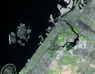 Satellite view of hundreds of small artificial islands arranged like a world map offshore from a gridded coastal city, with a palm-shaped island nearby.