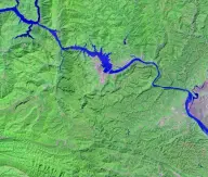 Satellite view of a wide river and long narrow reservoir winding through steep green terrain, with a straight dam and lock complex crossing the channel.