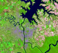 False-color satellite view of a broad branching reservoir behind a large dam on a north-south river, surrounded by bright green and pink farmland.